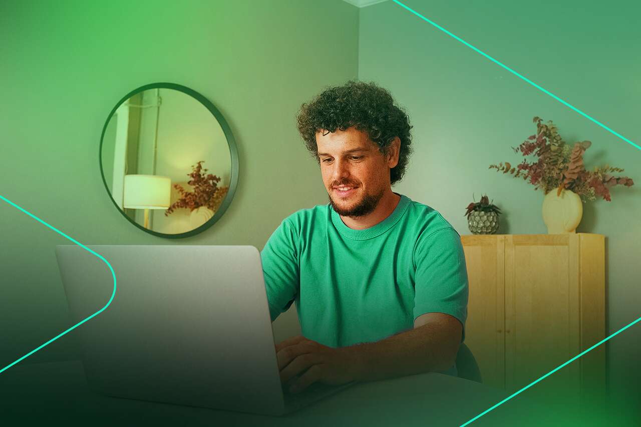 Homem sorrindo enquanto trabalha no laptop em casa.
