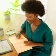 Mulher sorridente escrevendo em caderno na mesa.