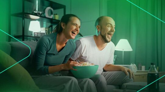 Casal sorrindo enquanto assiste filme e come pipoca.