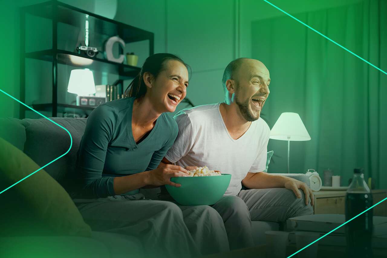 Casal sorrindo enquanto assiste filme e come pipoca.