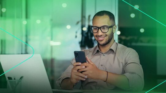Homem sorridente usando smartphone no trabalho.
