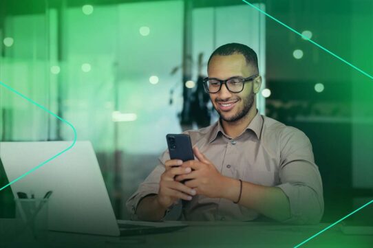 Homem sorridente usando smartphone no trabalho.