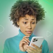 Jovem com cabelo cacheado usando celular com expressão de surpresa