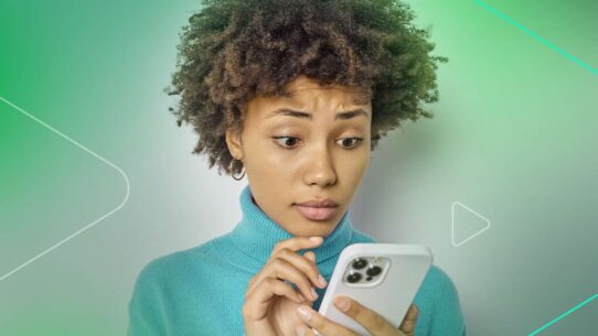 Jovem com cabelo cacheado usando celular com expressão de surpresa