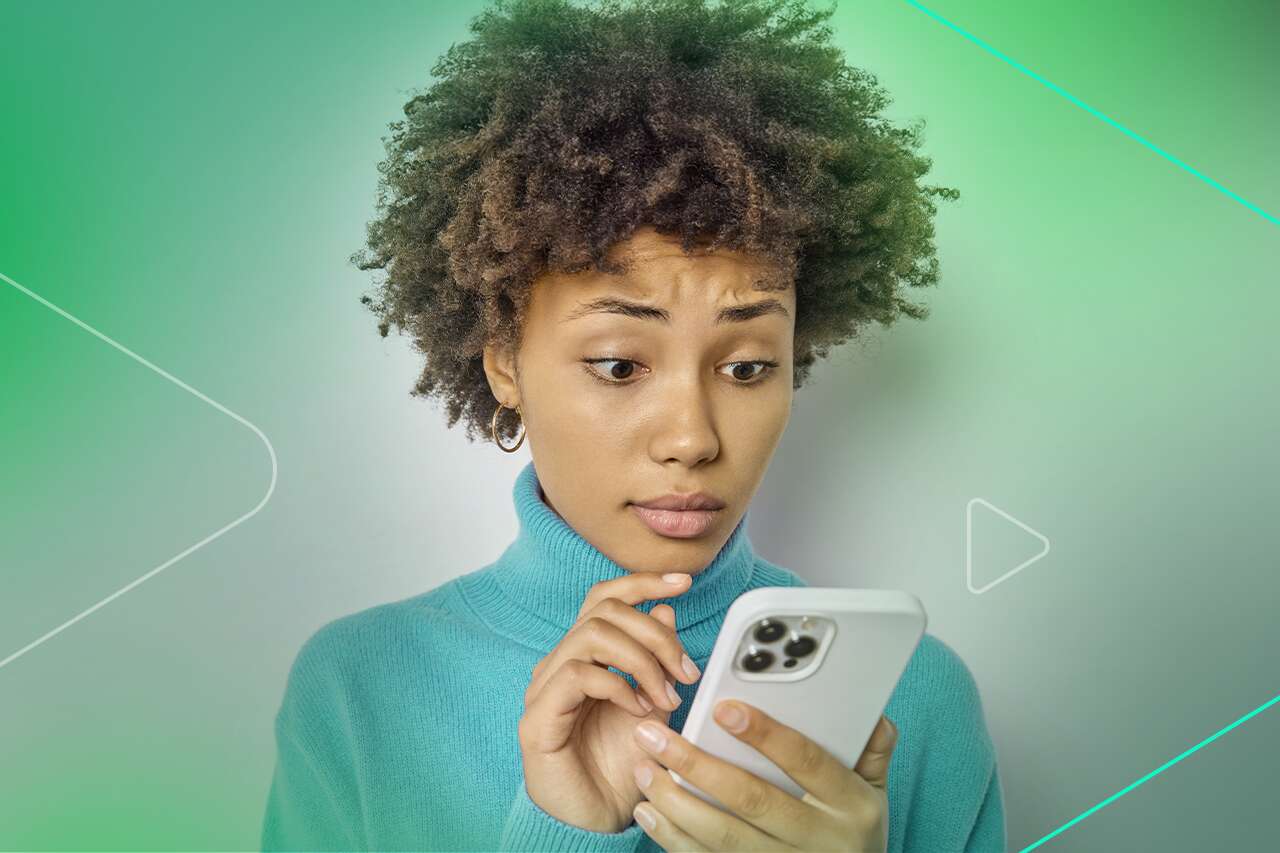 Jovem com cabelo cacheado usando celular com expressão de surpresa
