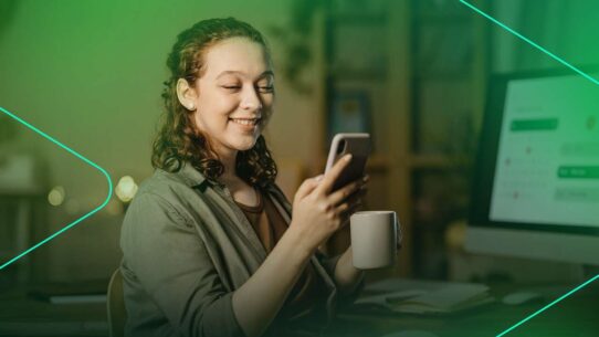 Jovem sorrindo enquanto usa o celular e segura uma xícara.