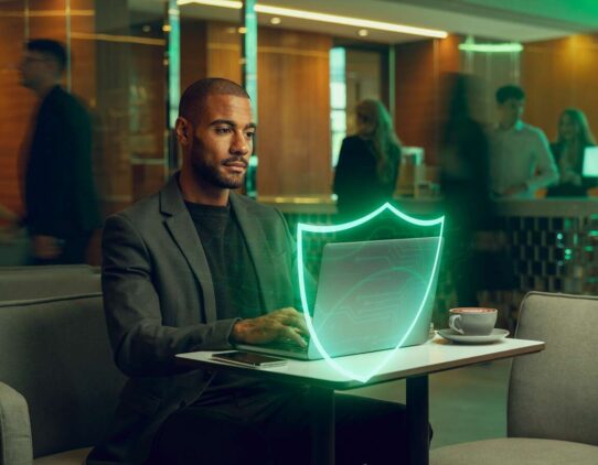 Homem trabalhando no laptop com proteção digital visível.