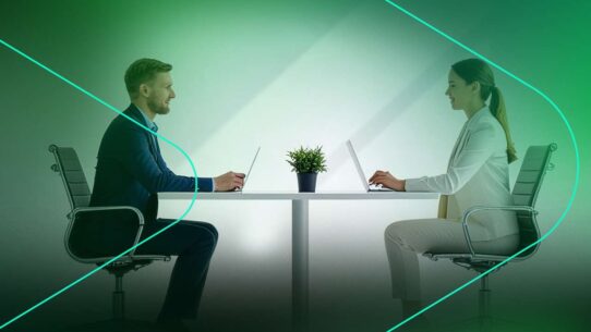 Dois profissionais em videoconferência em mesa de trabalho.