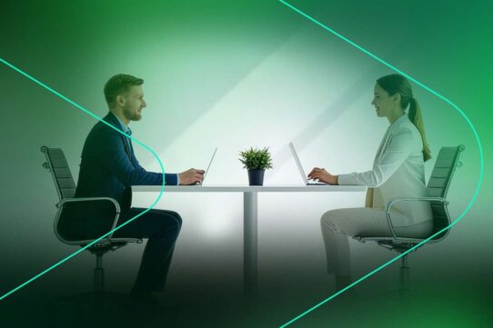Dois profissionais em videoconferência em mesa de trabalho.