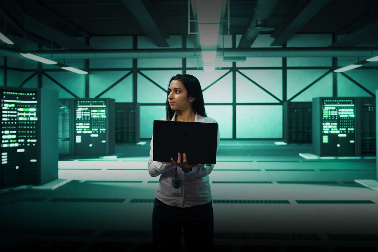 Mulher segura laptop em sala de servidores modernos.