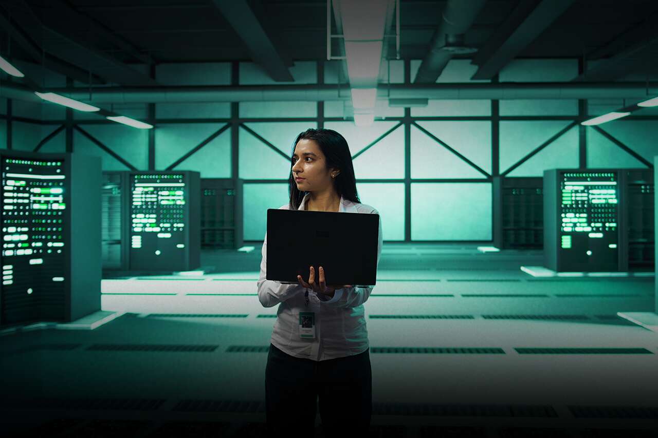 Mulher segura laptop em sala de servidores modernos.