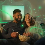 Casal sorrindo e assistindo filme com pipoca.