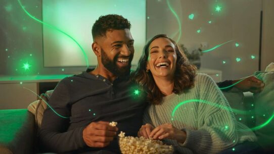 Casal sorrindo e assistindo filme com pipoca.