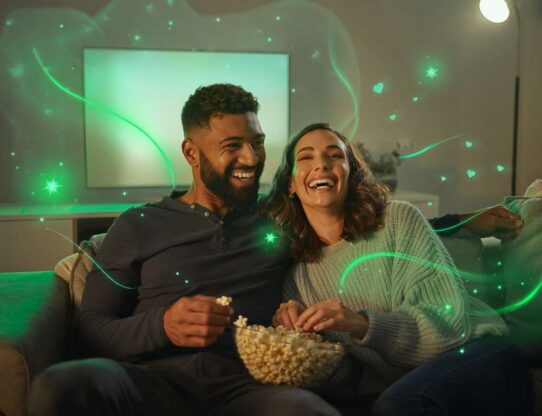 Casal sorrindo e assistindo filme com pipoca.