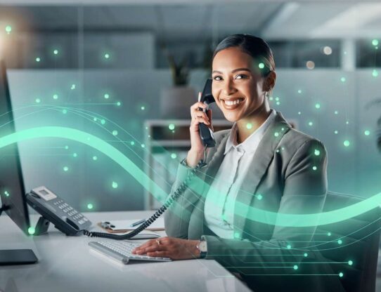 Mulher sorridente atendendo telefone em escritório moderno.