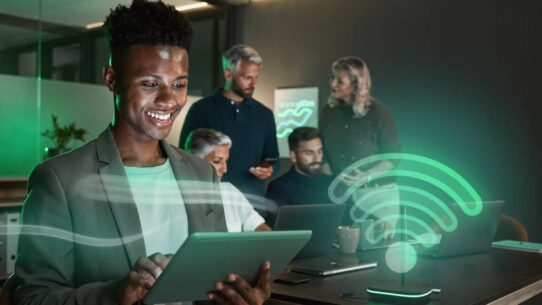 Homem sorrindo usando tablet em ambiente de trabalho moderno.