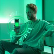 Homem avaliando bateria de smartphone em ambiente verde.