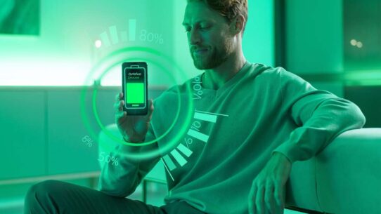 Homem avaliando bateria de smartphone em ambiente verde.