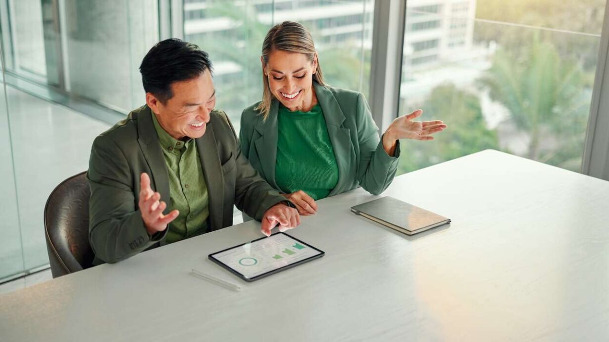 Casal sorridente analisando gráficos em um tablet.