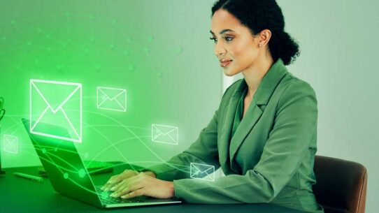 Mulher usando laptop com ícones de email em verde.